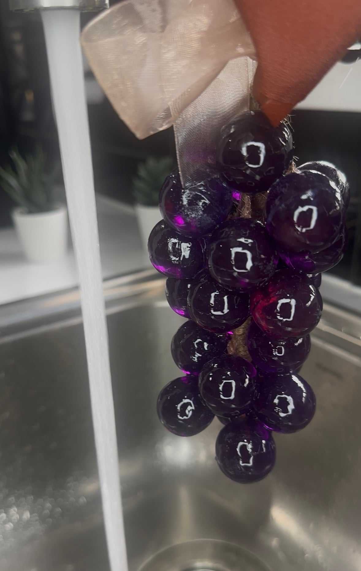 Handcrafted grape soap on a rope hanging near a running faucet in a kitchen sink